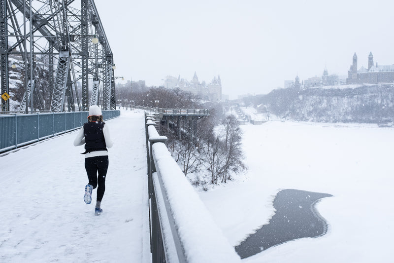 Foto einer jungen Frau welche über eine verschneite Brücke rennt